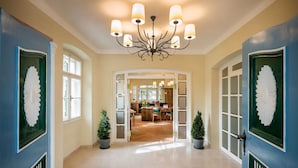 A hallway with a chandelier, potted plants, and a view into a dining area.