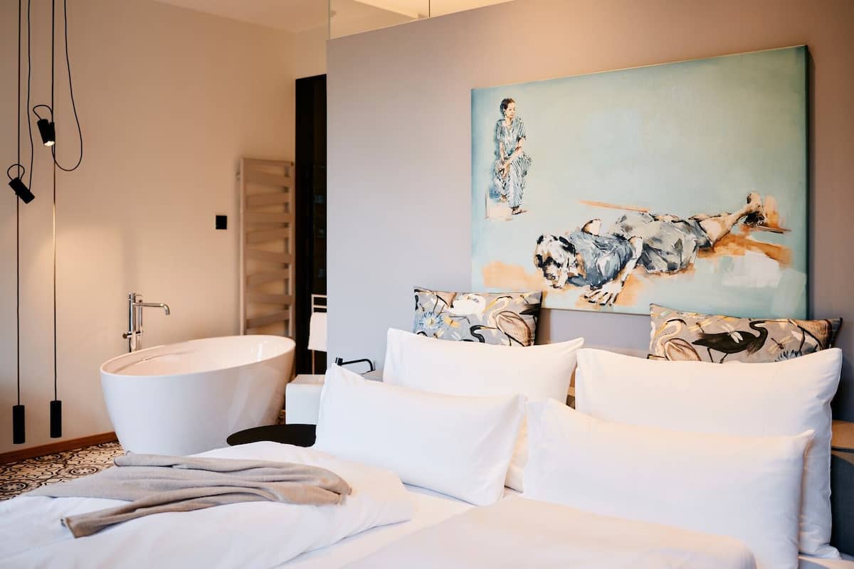Une chambre d’hôtel moderne avec un grand lit, une baignoire blanche et un tableau représentant des oiseaux accroché au mur.