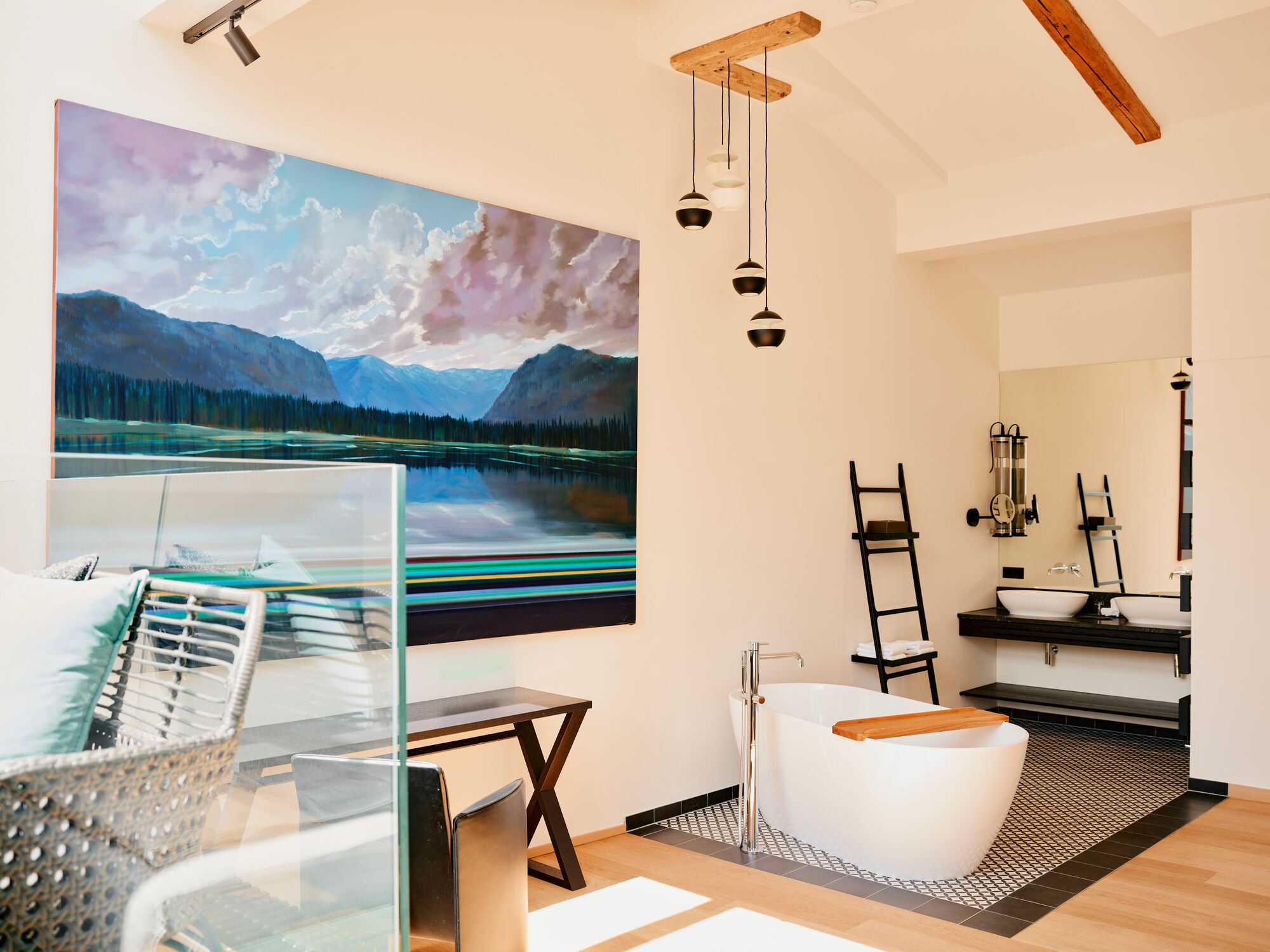 A modern bathroom with a bathtub, a large painting of a mountain landscape, and a glass partition.