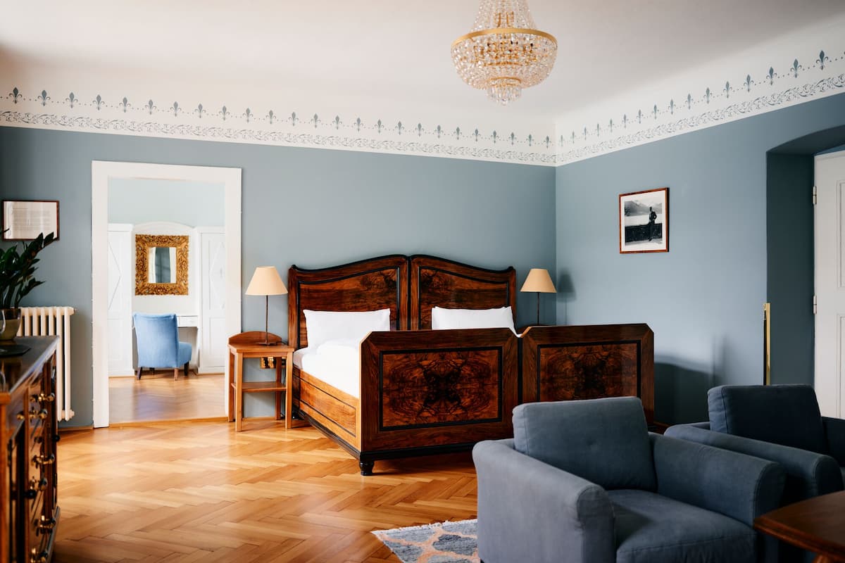Une chambre à coucher avec un lit en bois, deux tables de chevet, un lustre et un fauteuil bleu.
