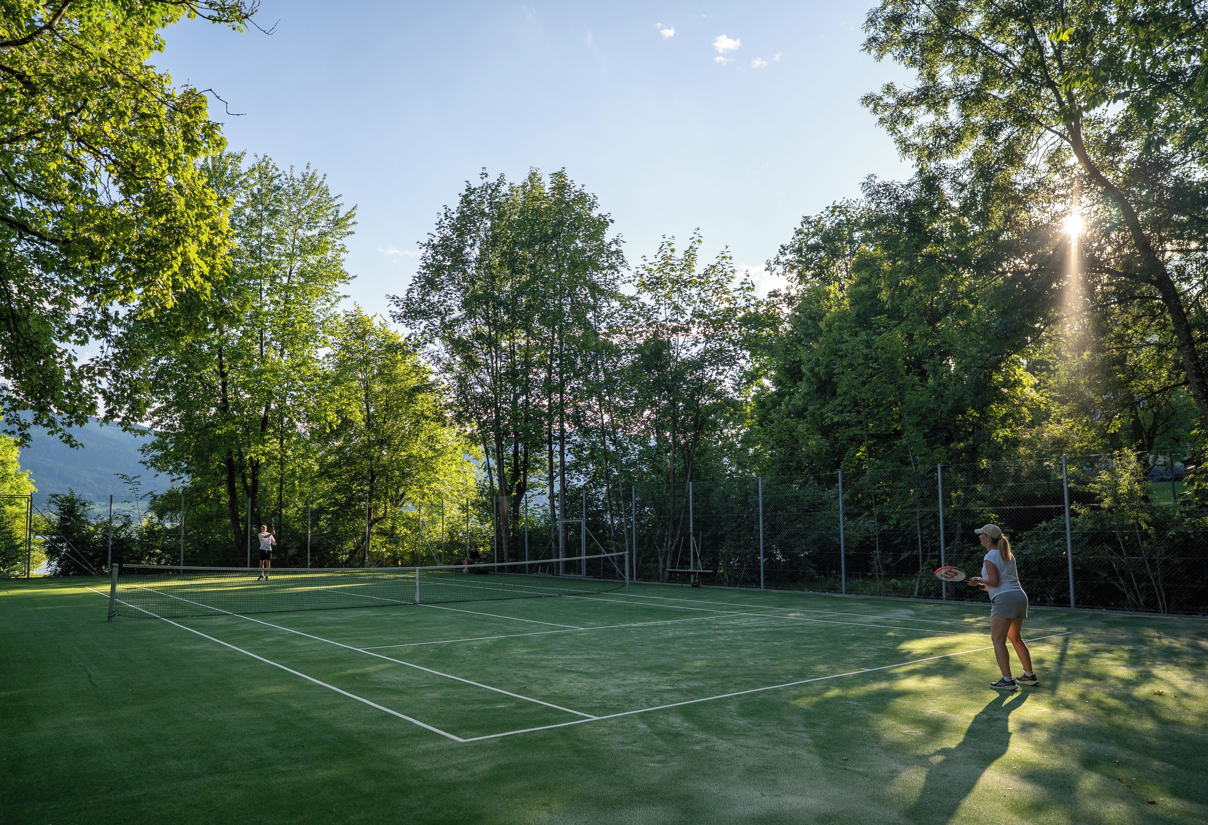 An outdoor tennis court surrounded by trees.