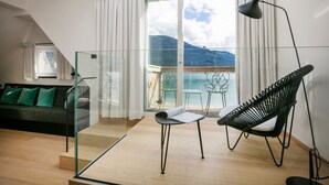 A modern living room with a glass partition, a sofa with green cushions, a black chair, and a view of the mountains through large windows.