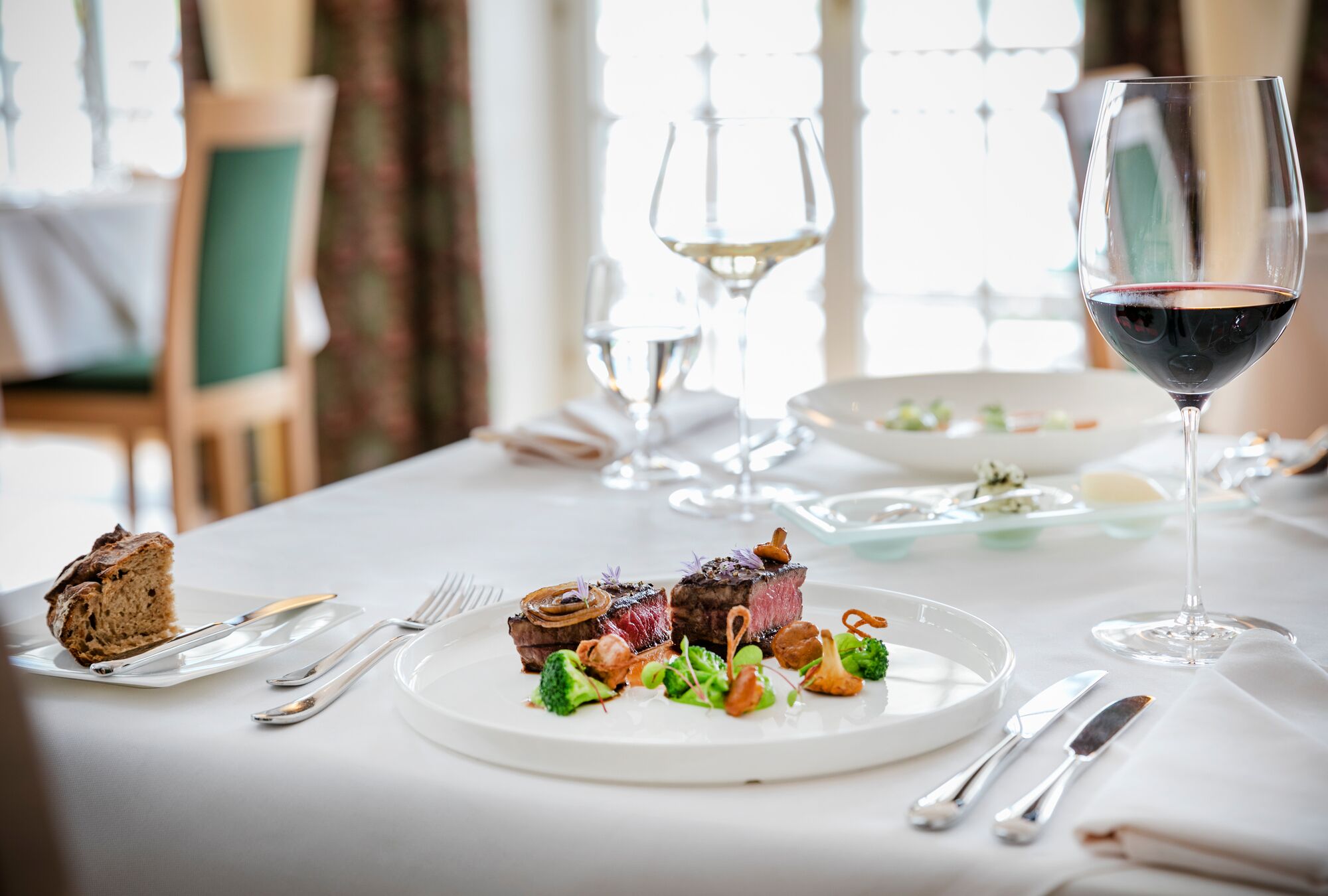 A dining table with a plate of food, wine glasses, and cutlery.