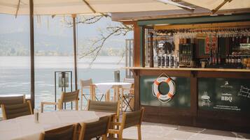 An outdoor bar area with a view of a lake, wooden tables and chairs, and a life ring decoration.