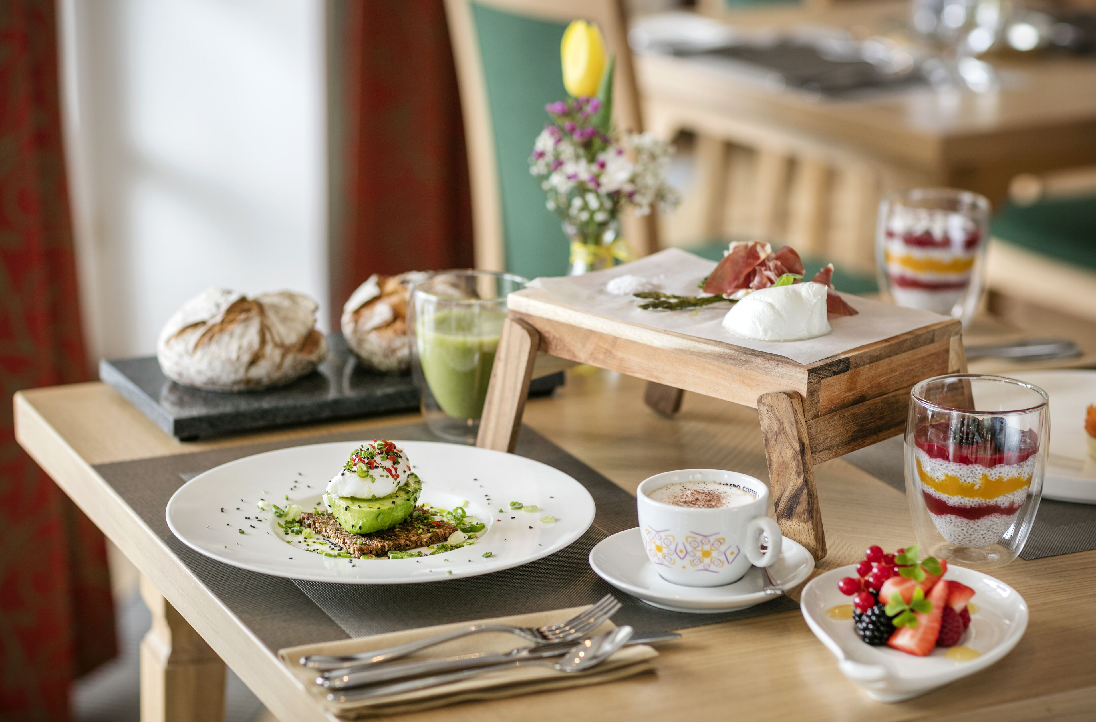 A breakfast setting with a plate of food, a cup of coffee, and a glass of layered dessert on a wooden table.