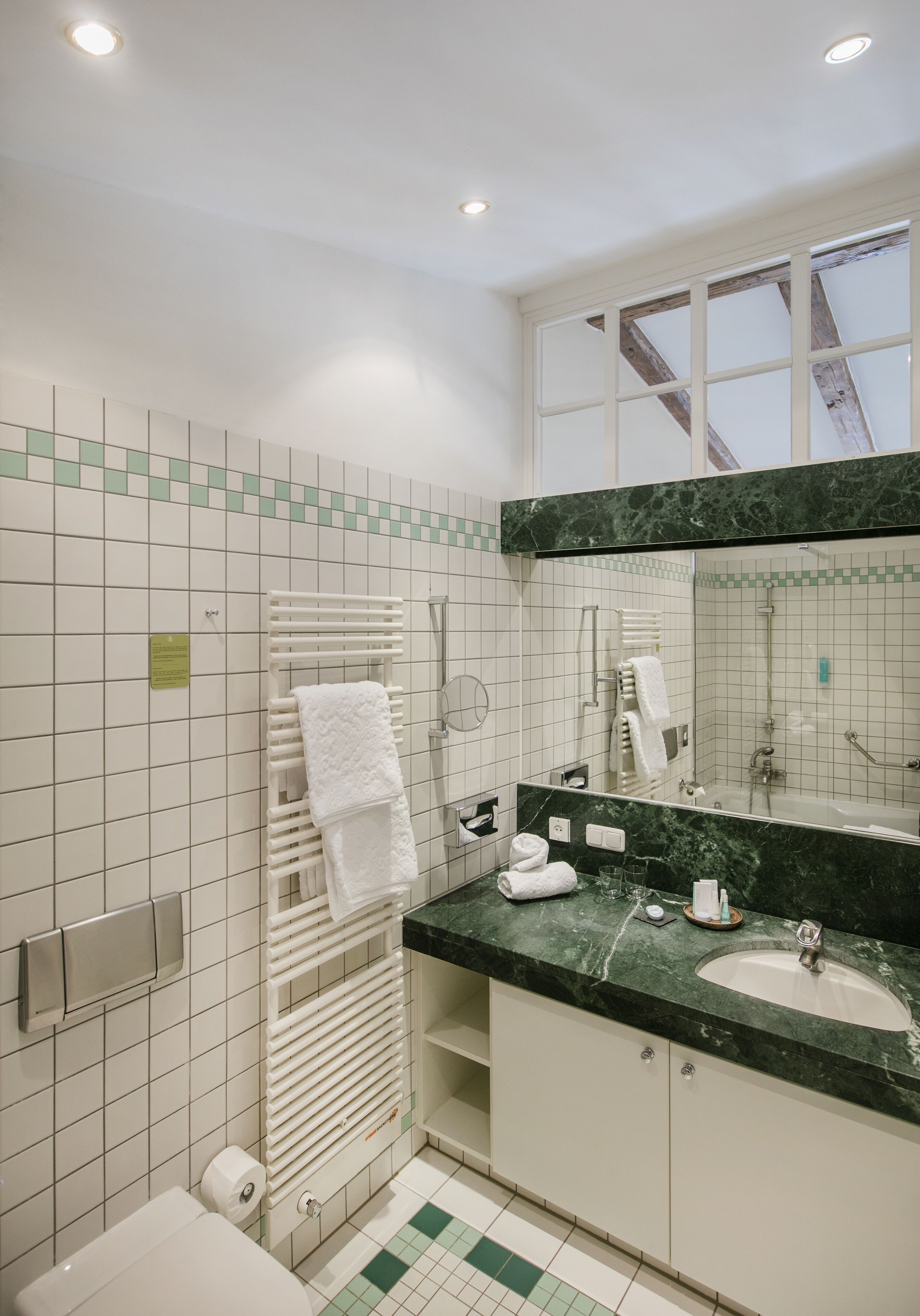 Ein Badezimmer mit Fliesenboden, einem Waschbecken, einem Spiegel und einem Handtuchhalter.