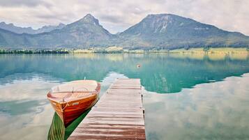 A wooden boat docked at a pier extending into a calm lake with mountains in the background.
