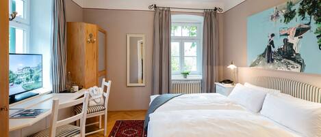 Habitación de hotel con cama, escritorio con computadora, silla, ventana con cortinas y un cuadro en la pared.