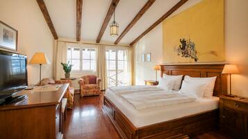 A hotel room with a wooden bed, a desk with a lamp, a chair, and a television.