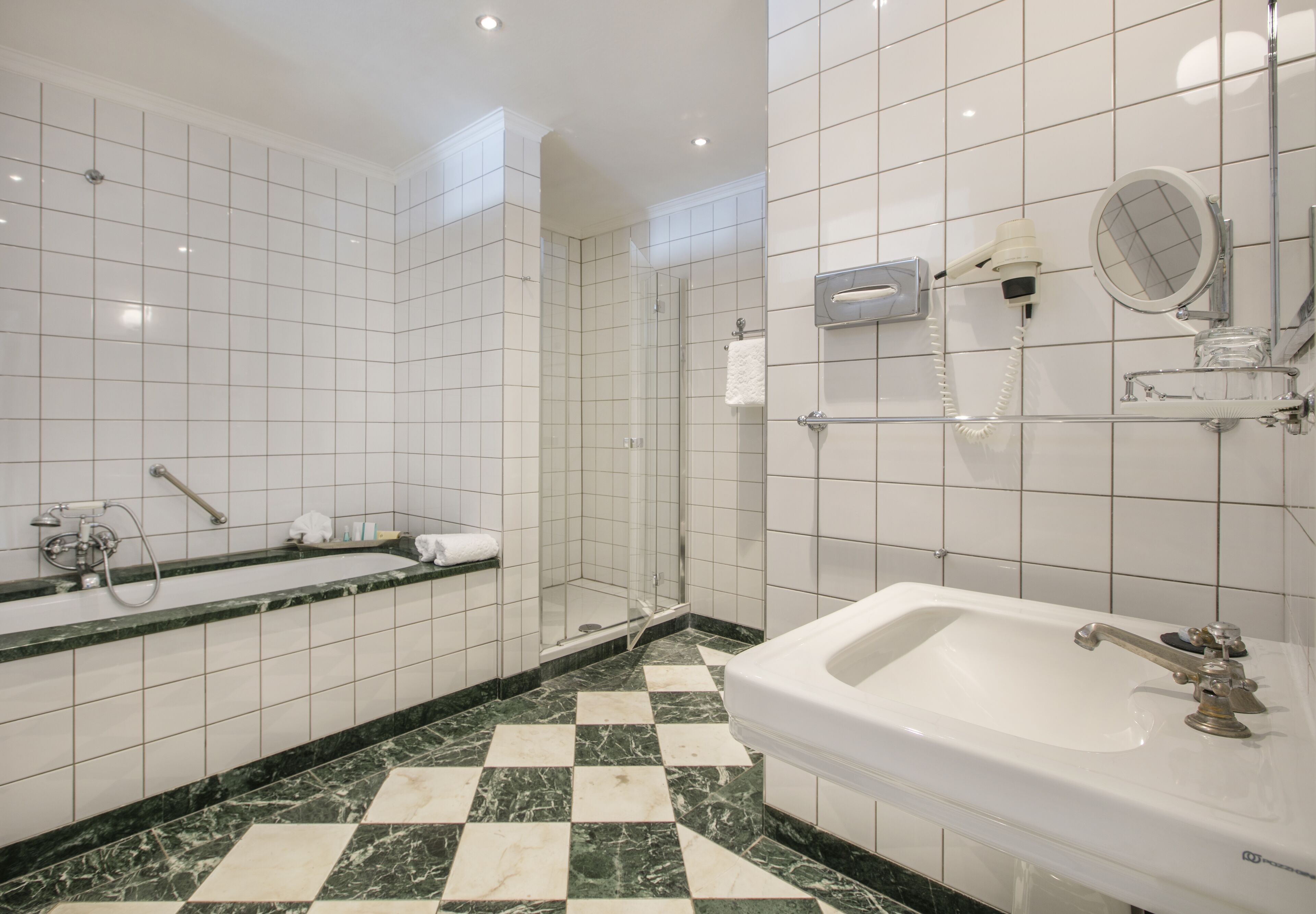 Une salle de bain avec un carrelage à motifs géométriques, une baignoire, une douche et un lavabo avec un miroir.