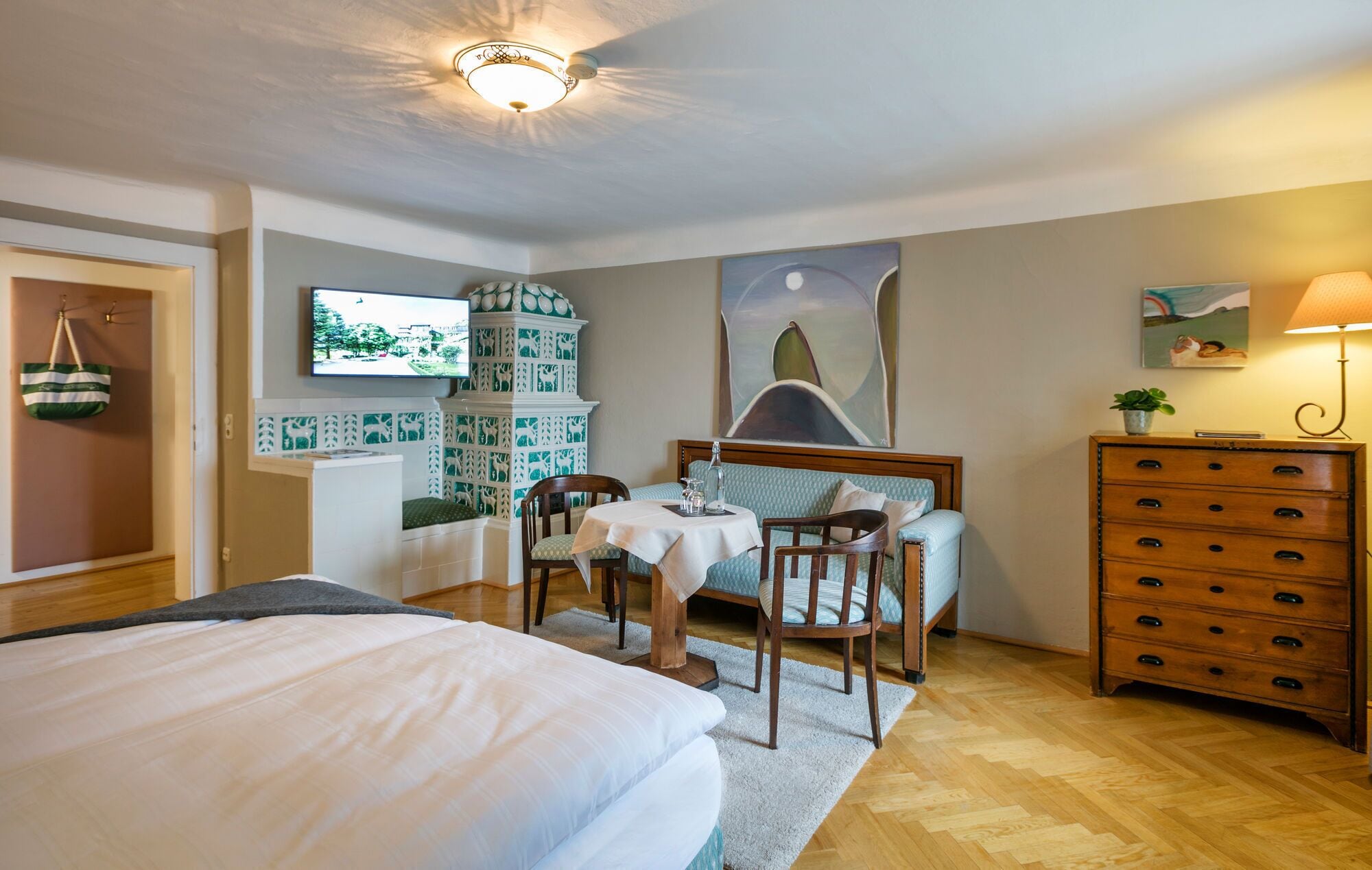 A hotel room with a bed, a dining table with chairs, a dresser, and a TV mounted on the wall.