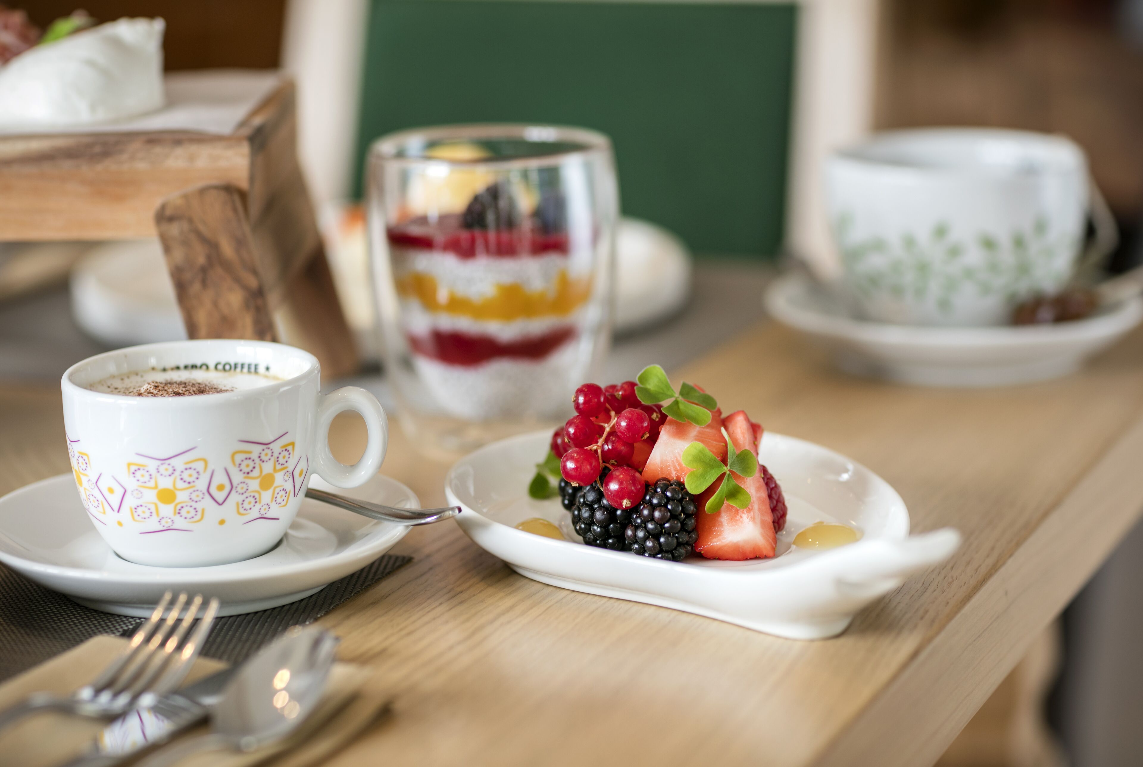 A table with a coffee cup, a layered dessert, and a fruit plate.