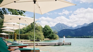 A lakeside resort with green lounge chairs and umbrellas, a dock, and mountains in the background.