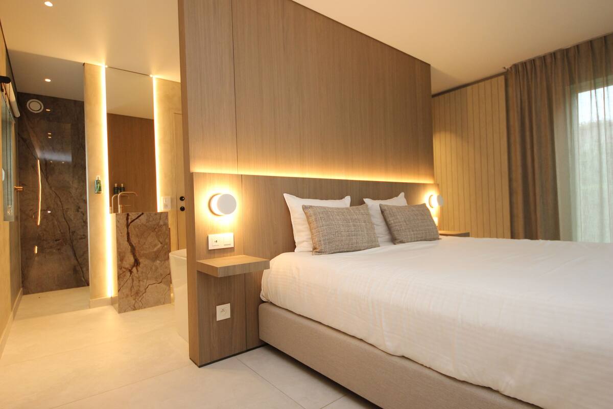 A modern hotel room with a large bed, wooden headboard, and bedside lamps.