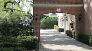 A brick archway with a speed limit sign, a paved pathway, and a building entrance with a white door and potted plants.
