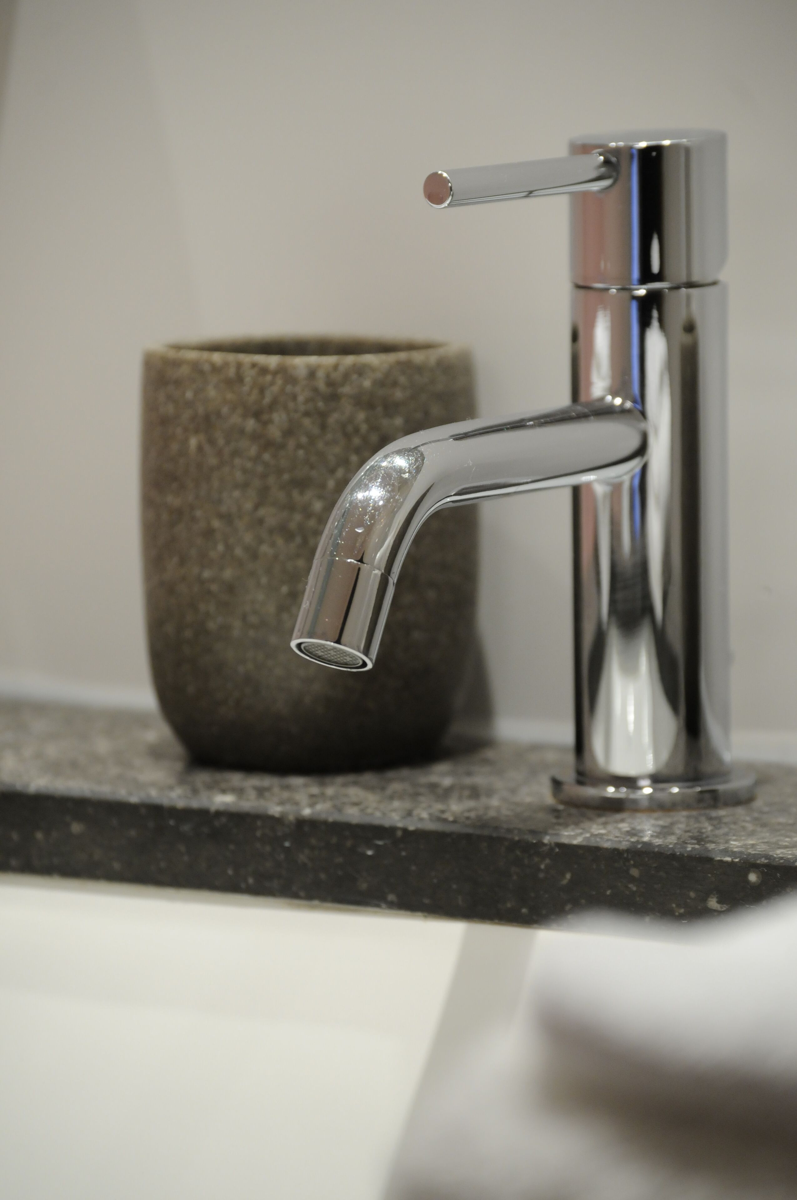 A modern bathroom with a chrome faucet and a textured stone container on the countertop.
