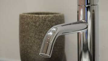 A modern bathroom with a chrome faucet and a textured stone container on the countertop.