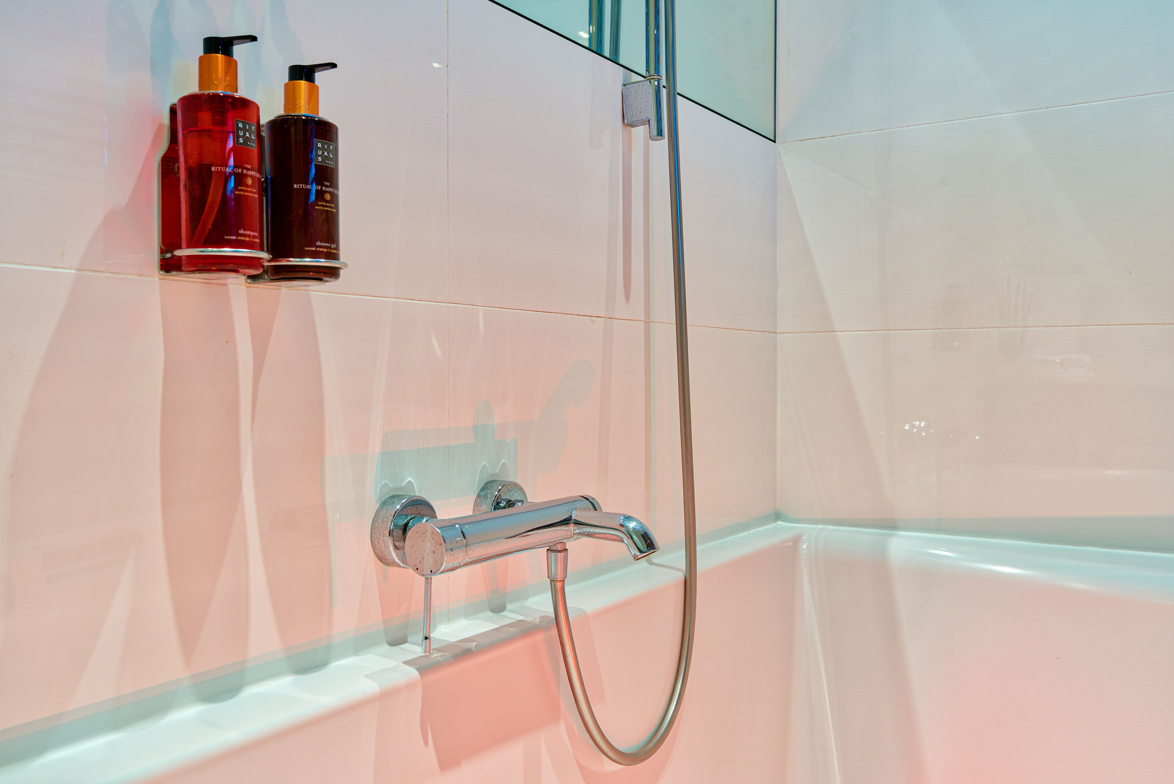 A bathroom with a bathtub, a shower, and two bottles of shampoo on the wall.