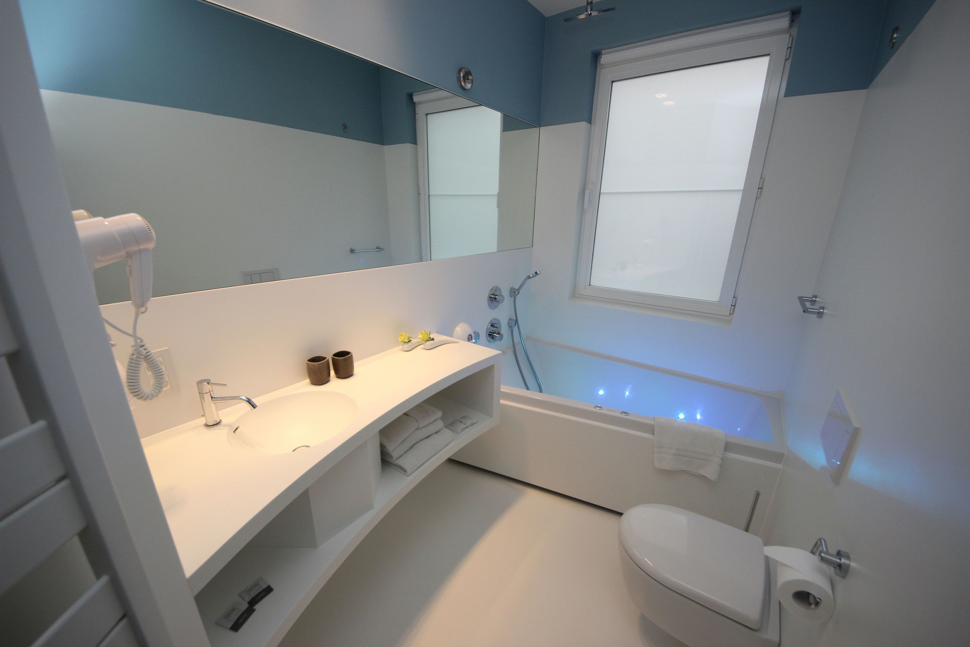 A modern bathroom with a white sink, mirror, and toilet. There is a towel rack and a shower area with a glass door.