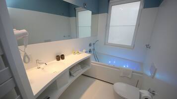 A modern bathroom with a white sink, mirror, and toilet. There is a towel rack and a shower area with a glass door.
