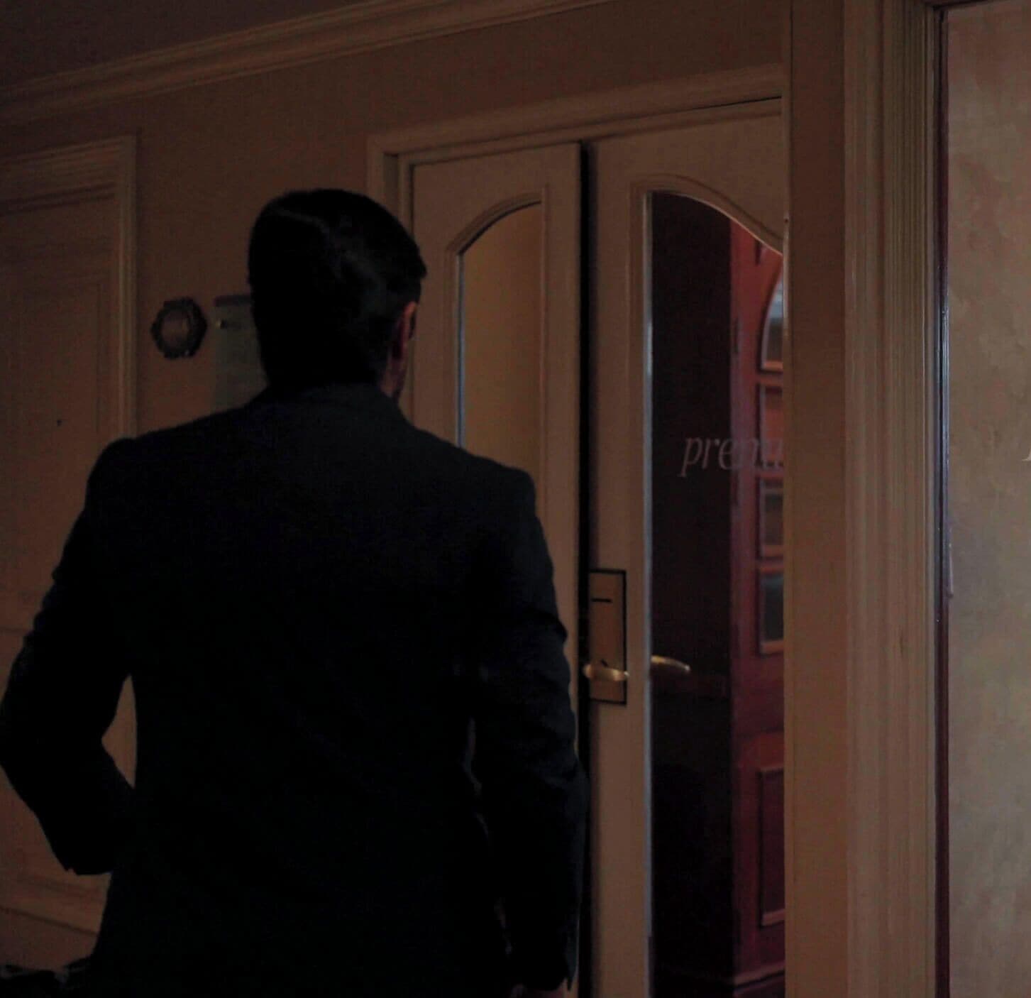 A person in a dark suit walking towards a door with a glass panel.