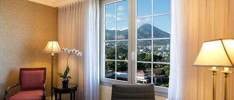 Habitación de hotel con un ventanal grande que ofrece vistas a la montaña, un escritorio con lámpara, una silla y una mesita con una planta en maceta.