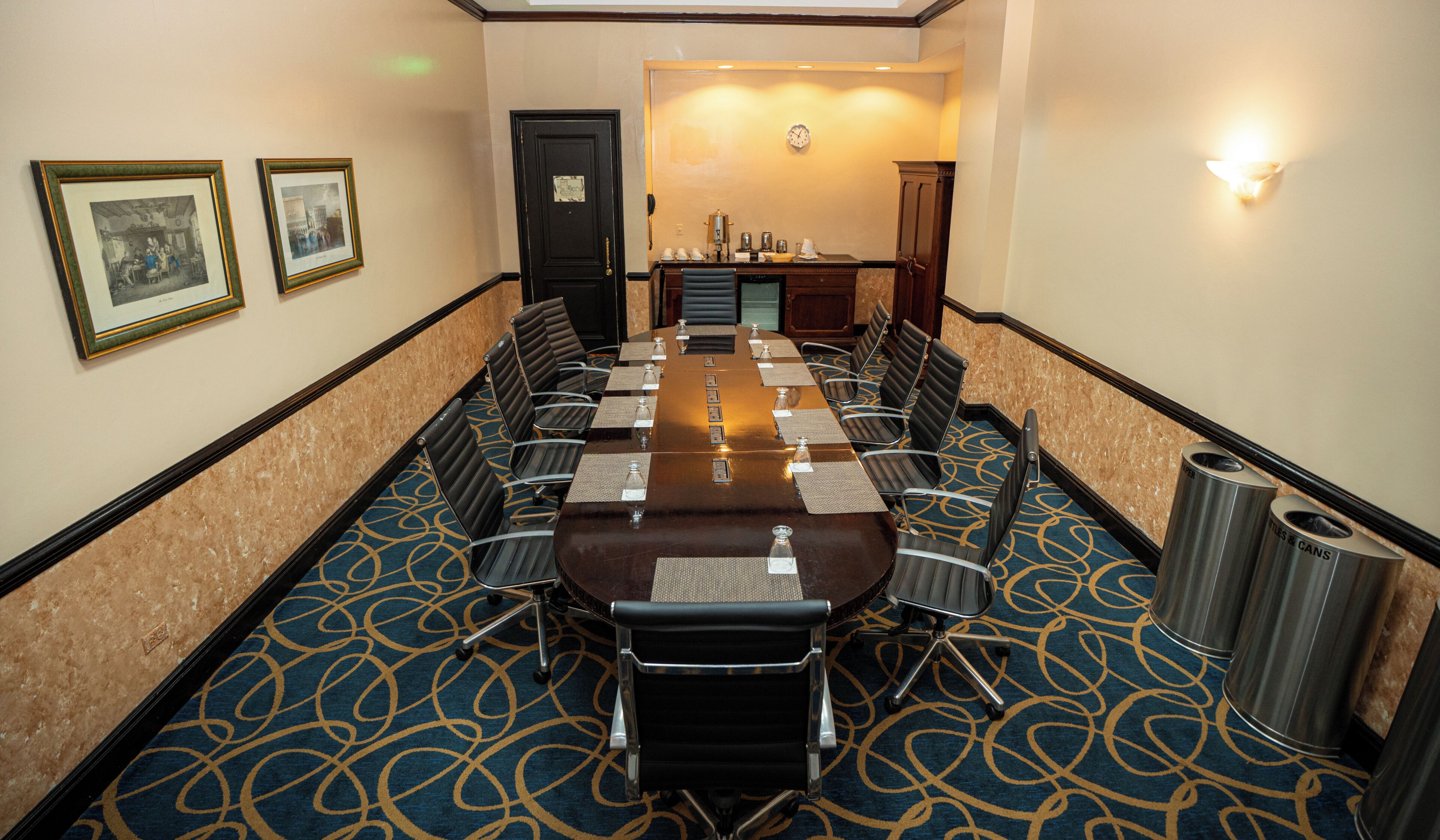 A conference room with a long table, chairs, a clock, and framed pictures on the wall.