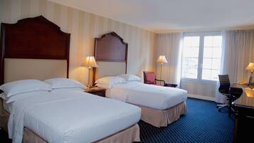 A hotel room with two beds, a desk, a chair, and a window with curtains.