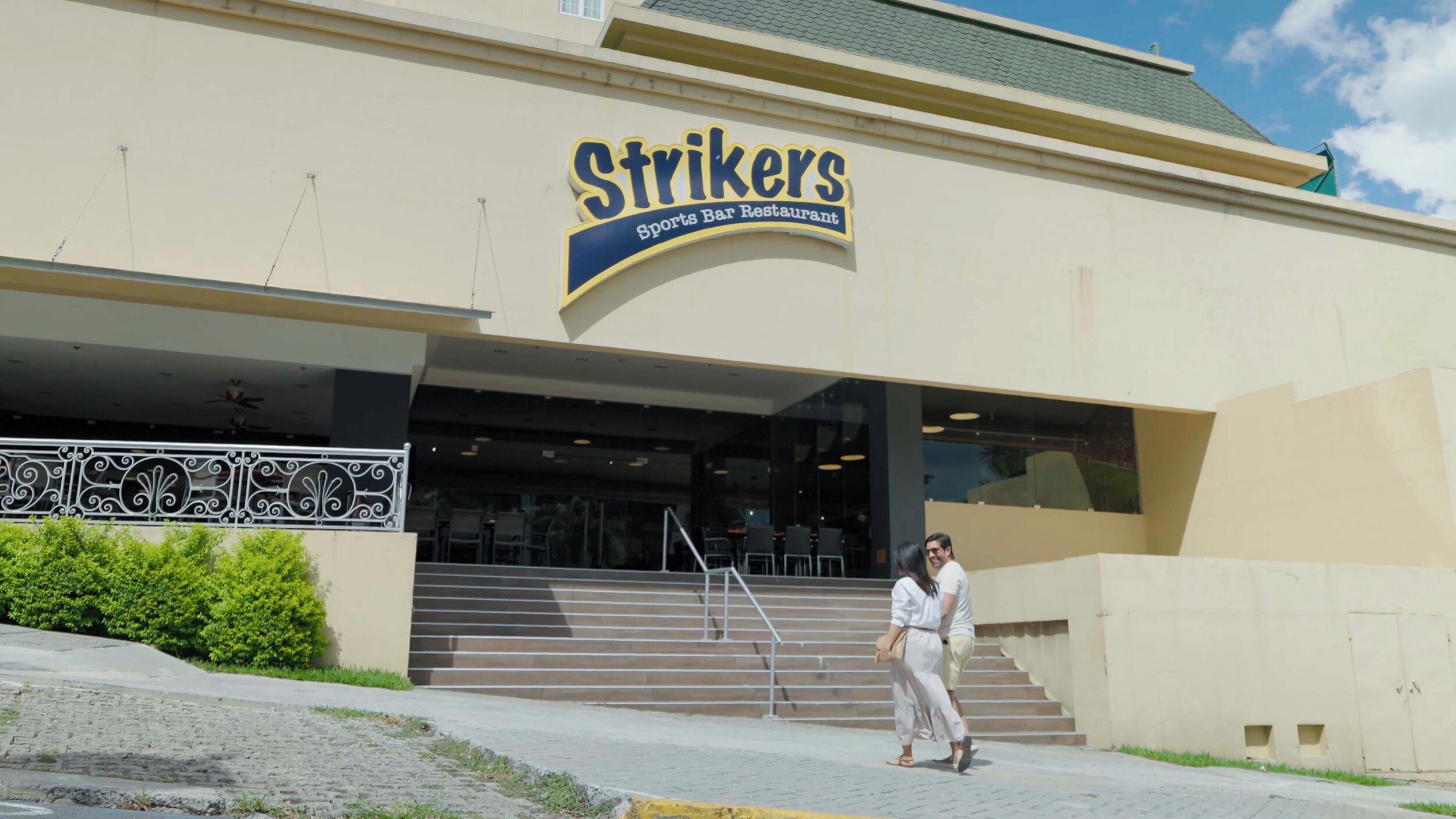 Un bâtiment sur lequel on peut lire l’inscription « Strikers Sports Bar Restaurant », et un escalier menant à l’entrée.