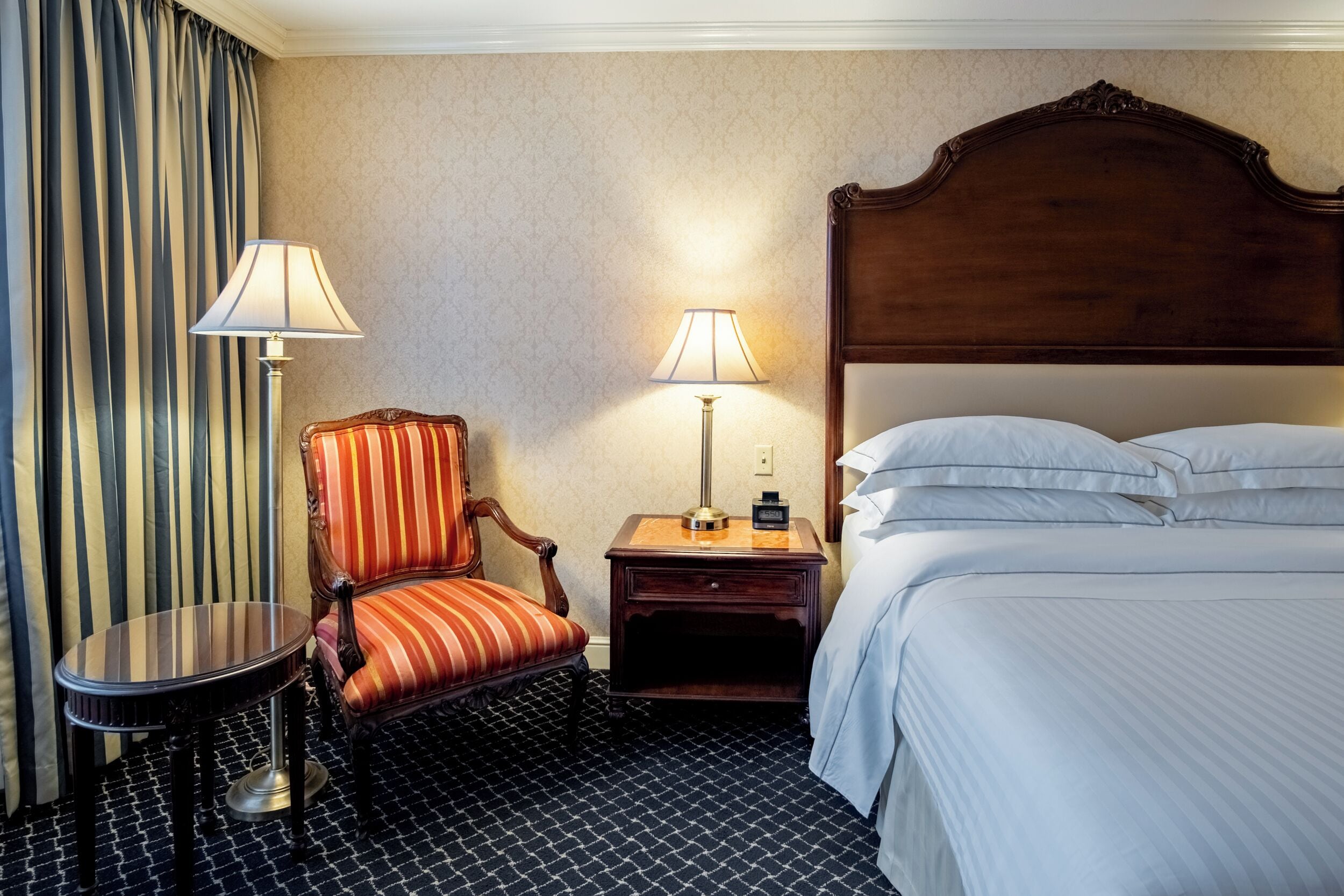 Une chambre d’hôtel avec un lit, deux lampes de chevet, une chaise, une petite table et une table de chevet.