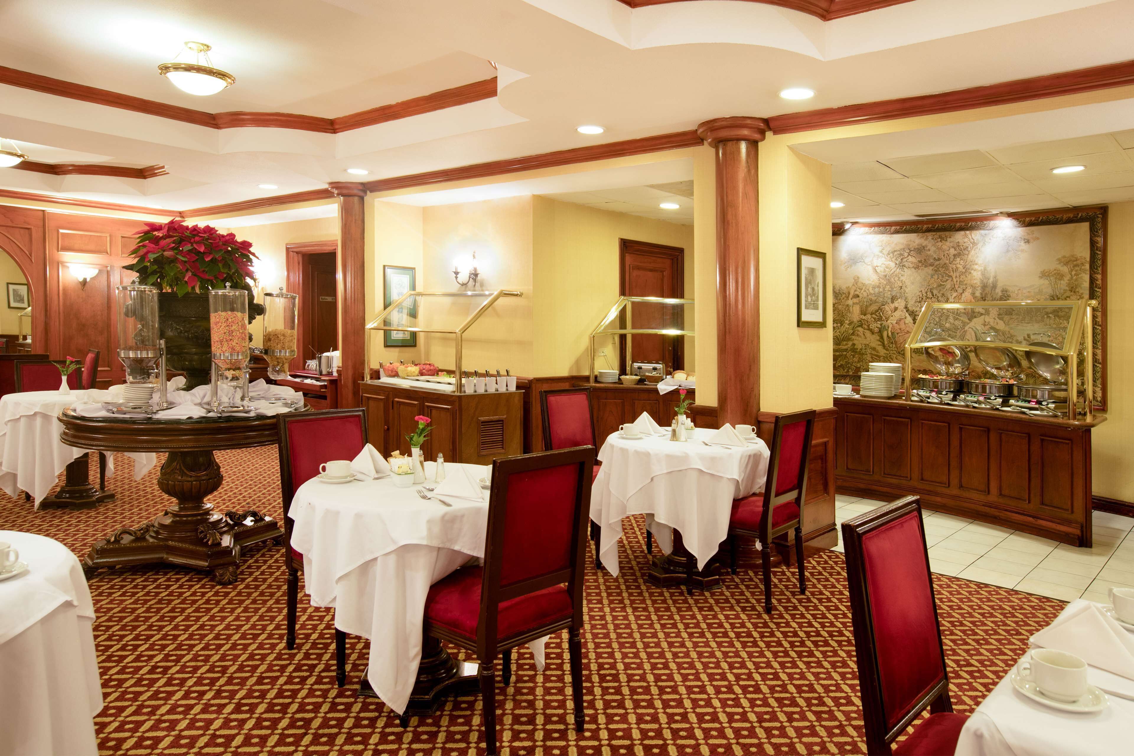 A hotel dining area with tables set for service, a buffet station, and a decorative wall with a floral pattern.