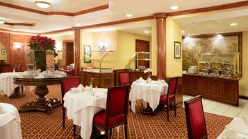 A hotel dining area with tables set for service, a buffet station, and a decorative wall with a floral pattern.