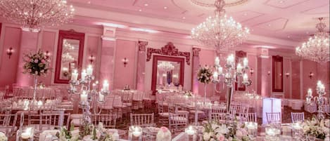 Un salón de banquetes con mesas redondas dispuestas para un evento formal, con candelabros y centros de mesa florales.