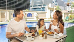 A family dining by a poolside with a view of modern buildings. - Barceló San Salvador (San Salvador)