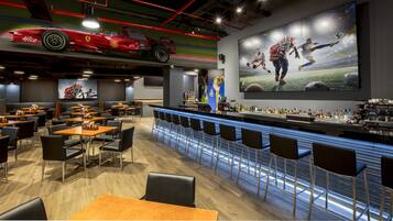 Un restaurante con una zona de bar, arte mural con temática deportiva y un modelo de coche Ferrari en el techo.