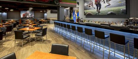 A restaurant with a bar area, sports-themed wall art, and a Ferrari car model displayed on the ceiling.