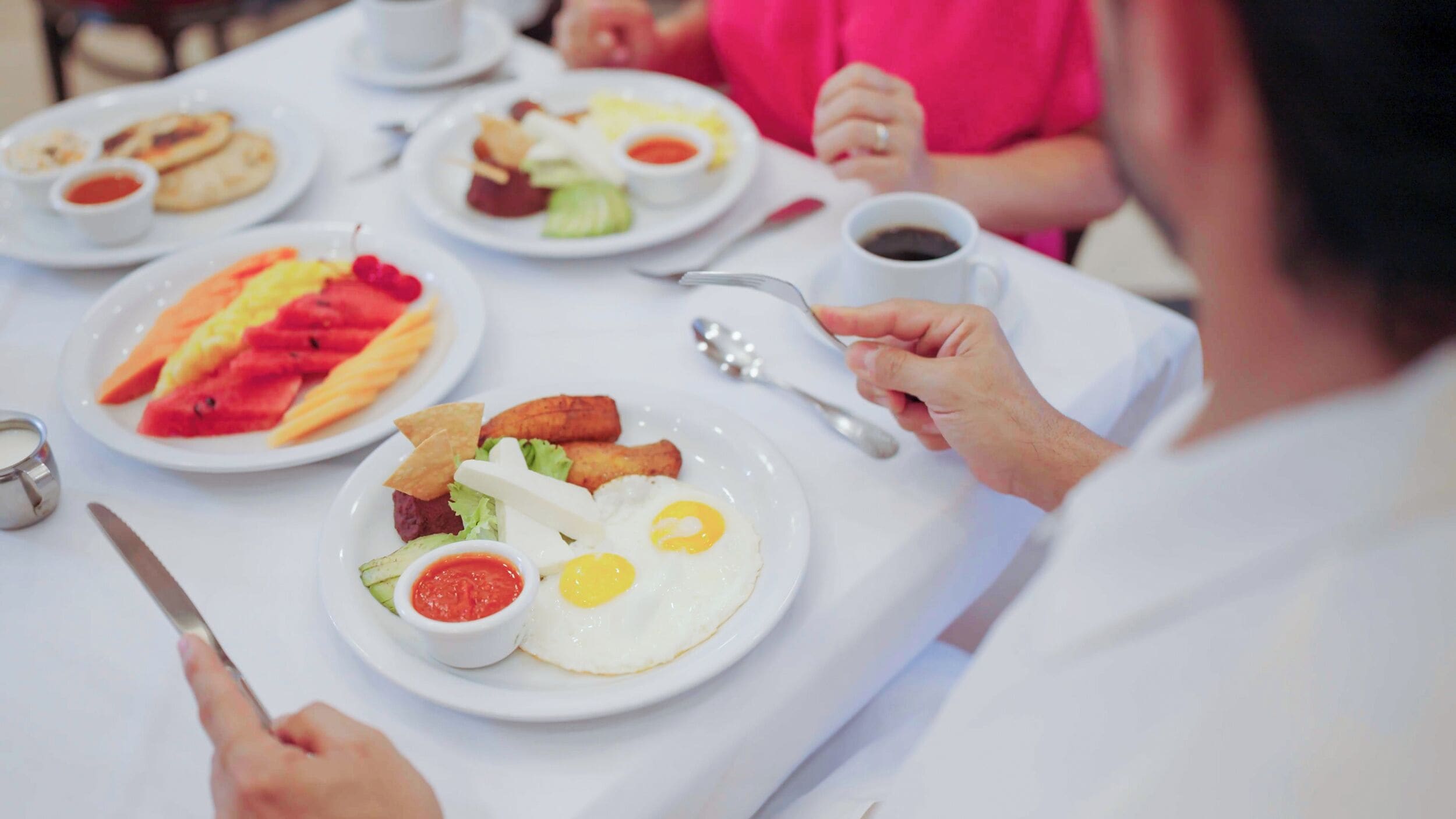 A dining table with plates of food, a cup of coffee, and a fork.