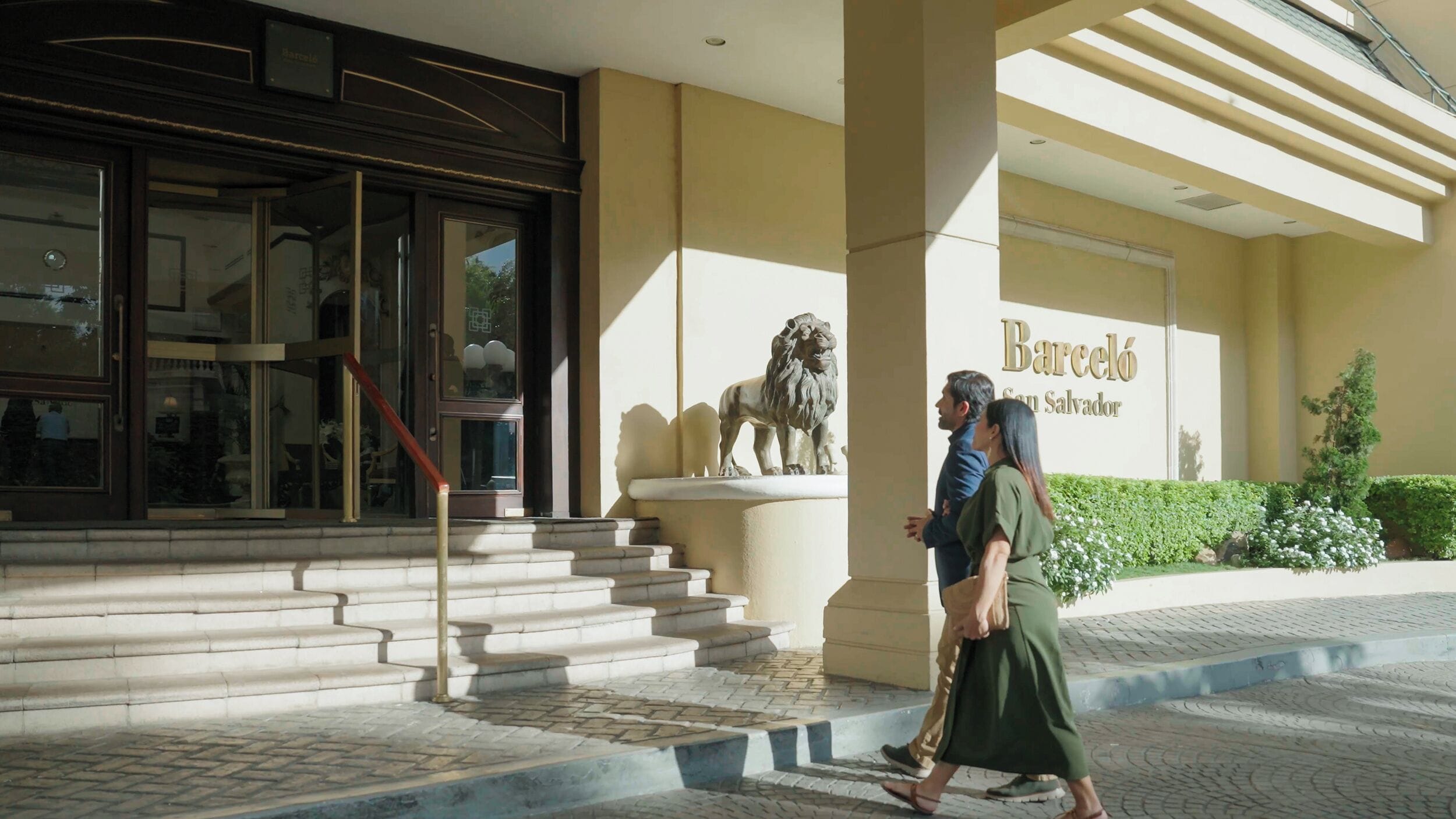 A building entrance with a lion statue, a staircase, and a sign reading 'Barceló San Salvador.'