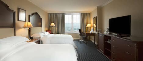Habitación de hotel con dos camas, un escritorio, televisión y vista a la ciudad por la ventana.