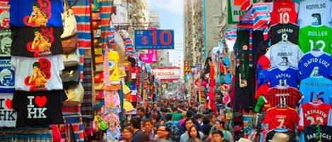 Un mercado callejero concurrido con varios puestos y letreros, incluyendo un cartel destacado con el precio de $10.