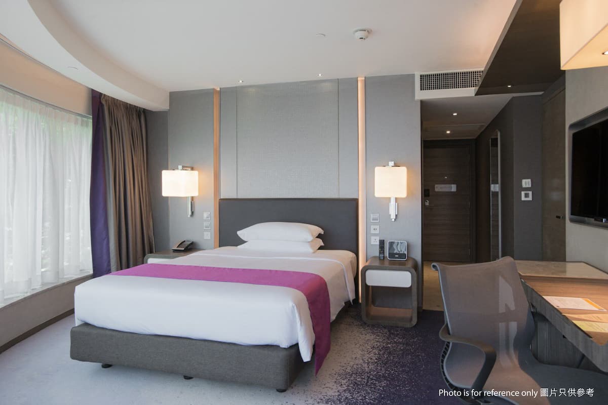 A modern hotel room with a large bed, bedside tables, a desk, and a TV.