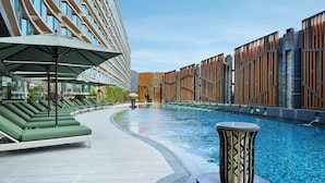 A poolside area with lounge chairs and umbrellas, a pool, and modern buildings in the background.