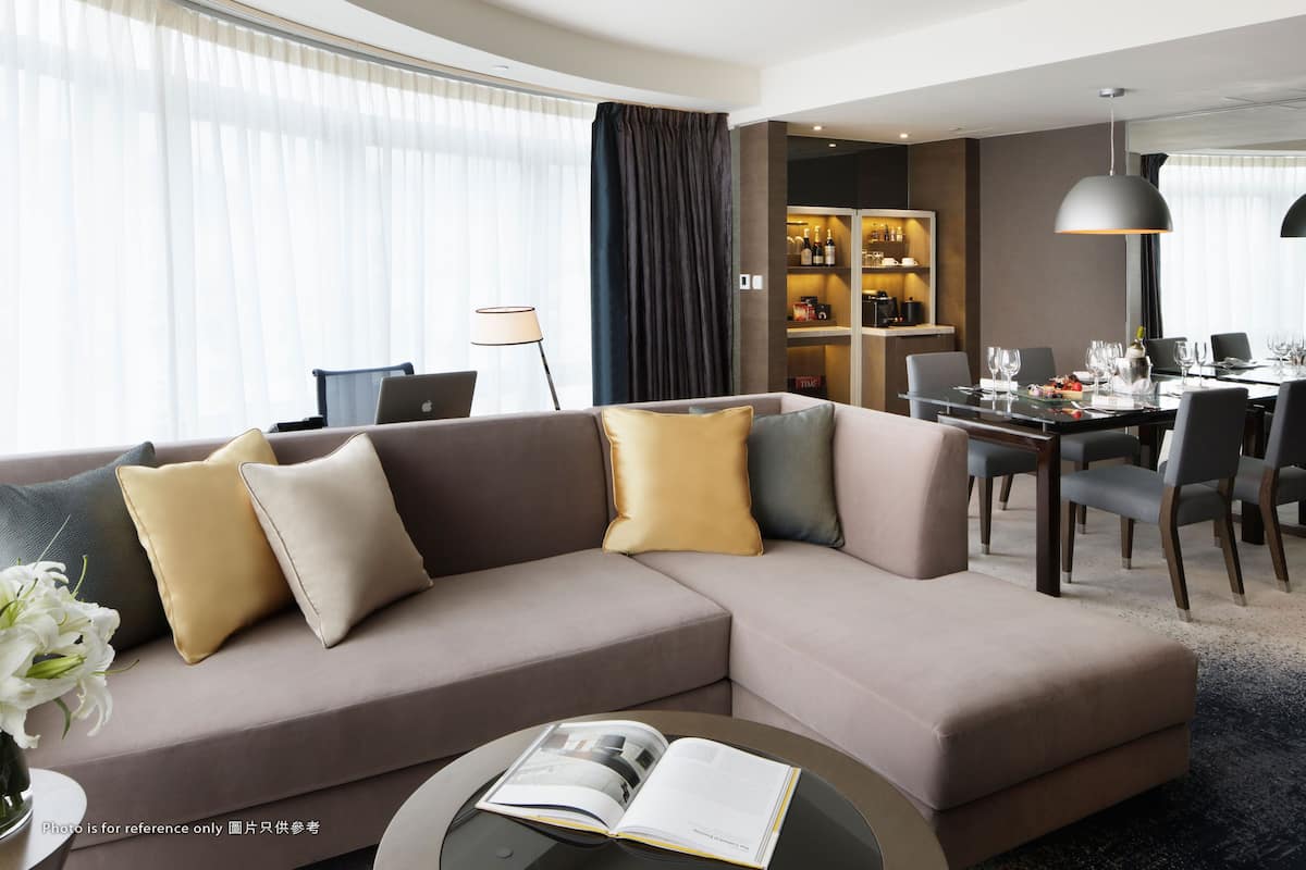 A modern living room with a sectional sofa, a dining area with a table set for six, and a bar area with shelves of bottles.