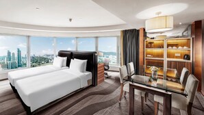 A modern hotel room with a large bed, a dining table, and a view of the city.