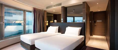 Habitación de hotel con dos camas, ventanas amplias, vista a la ciudad y una puerta de color oscuro.