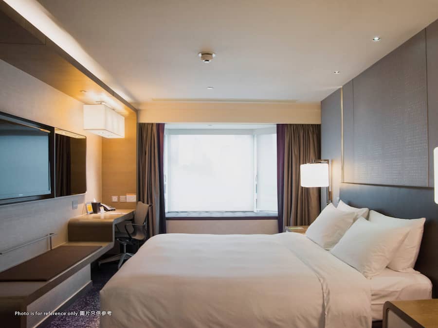 A hotel room with a large bed, a desk, a chair, a TV, and a window with curtains.