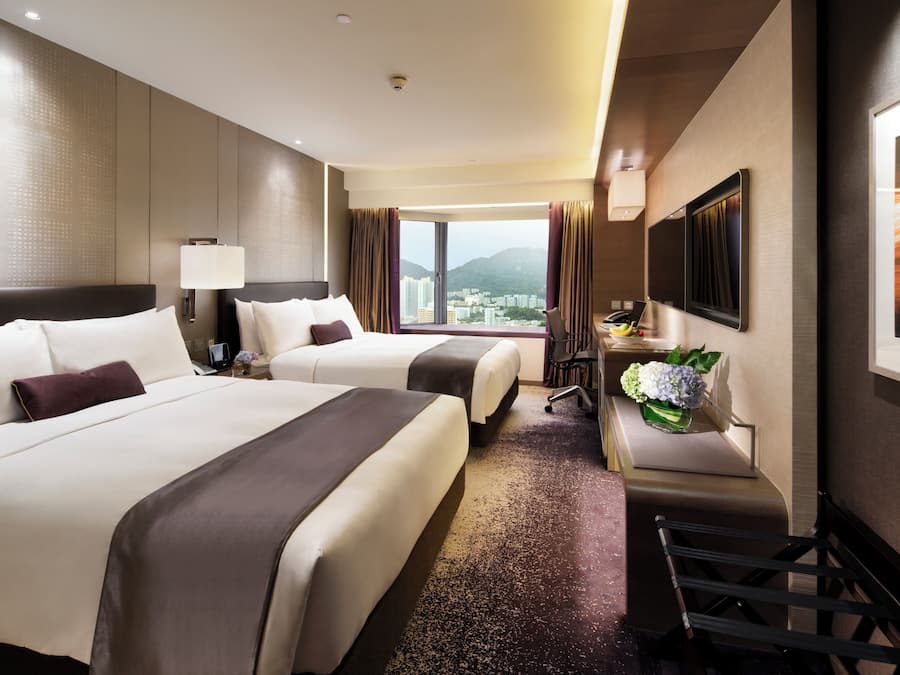 A hotel room with two beds, a desk, a chair, a TV, and a view of the city.