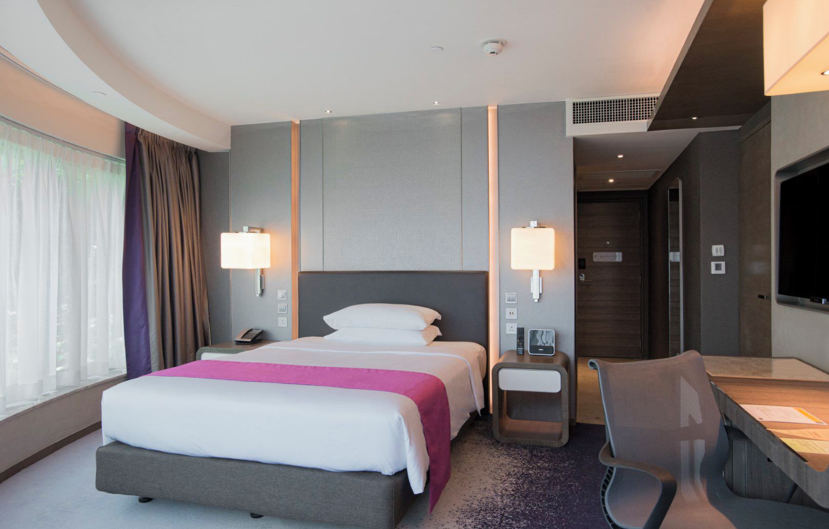 A modern hotel room with a large bed, bedside tables, a desk, and a TV.