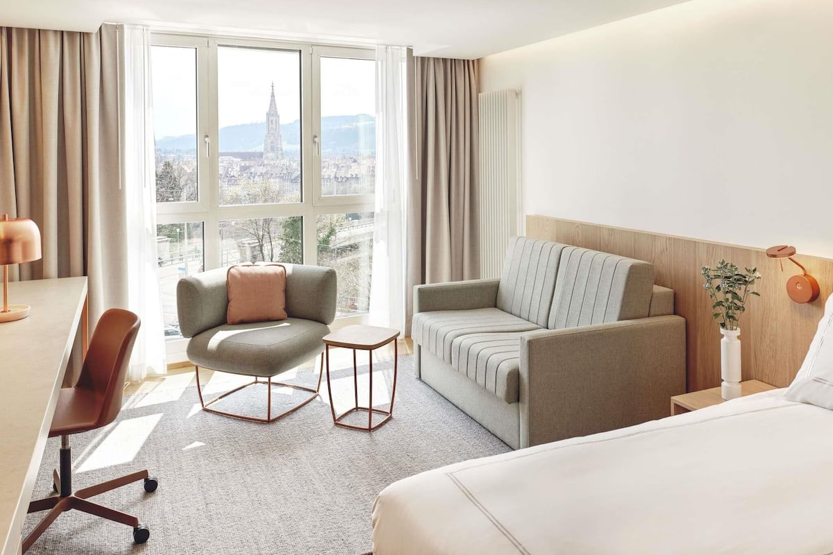 A hotel room with a bed, two sofas, a desk, and a chair.