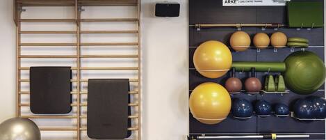 Un gimnasio con equipo de ejercicio, que incluye una barra de dominadas, balones medicinales y un estante fijado a la pared.